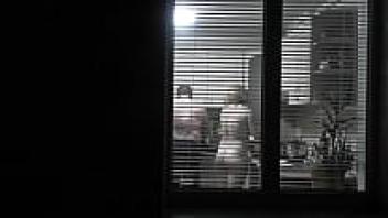 Looking in. A voyager. While the nude and attractive neighbor in the kitchen is preparing dinner for her spouse, the neighbor pervert voyeur is standing on the street in the evening and looking out the window. in public while naked. Nude when at home. As a family, outside