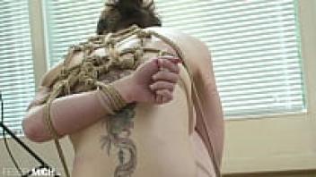 A gorgeous naked woman with little breasts is seen in a bondage while it is being created in a studio.